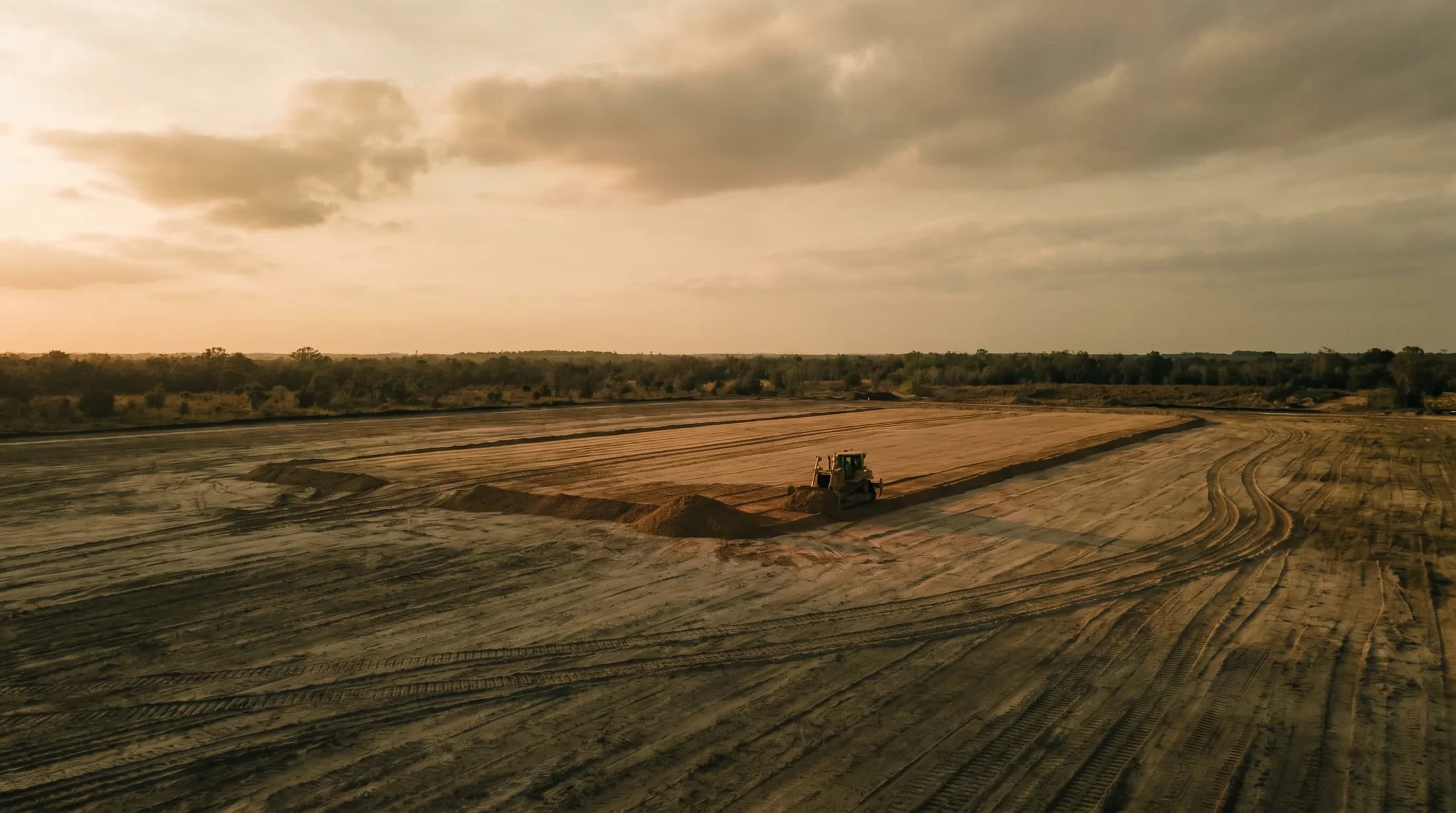 Heavy equipment grading raw land at golden hour